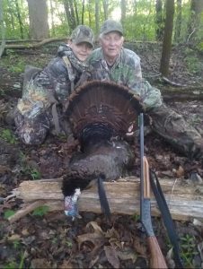 "Roscoe Spaulding and his granddaughter wearing camouflage gear, standing together in a wooded area, representing their bond through turkey hunting."