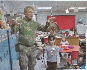 "A young Roscoe Spaulding in hunting attire, teaching in an elementary school classroom."