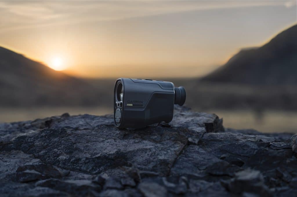 Garmin action camera resting on rugged rocks at sunset with a blurred mountain backdrop for the garm xero l60i rangefinder review.