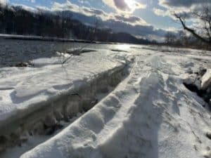 Snow-covered riverbank and thick ice shelves along the Salmon River during winter.