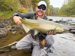 Stuart Wright kneeling in shallow river water while holding a large salmon.